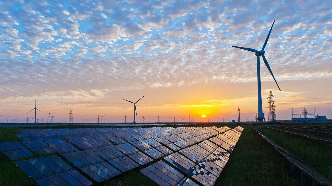 Solar panels and wind turbines at sunset represent Tetra Tech renewable energy engineering