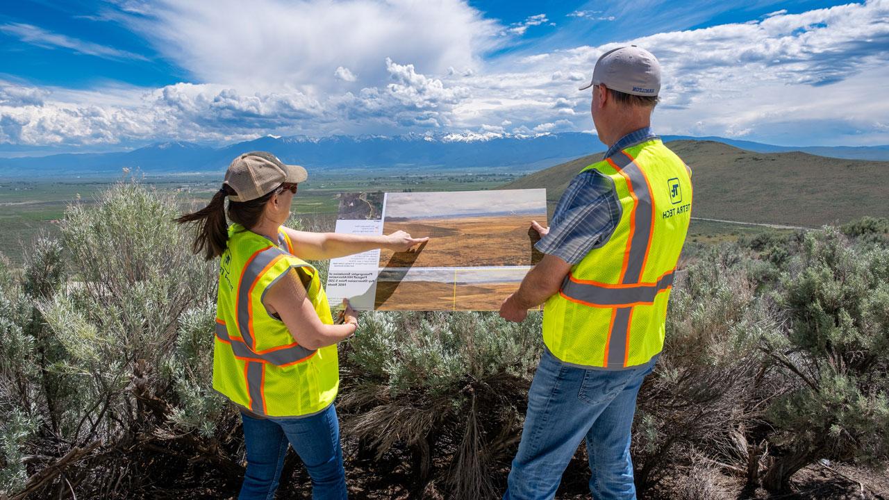 Two workers wearing hats and safety vests reviewing photo simulations in the field